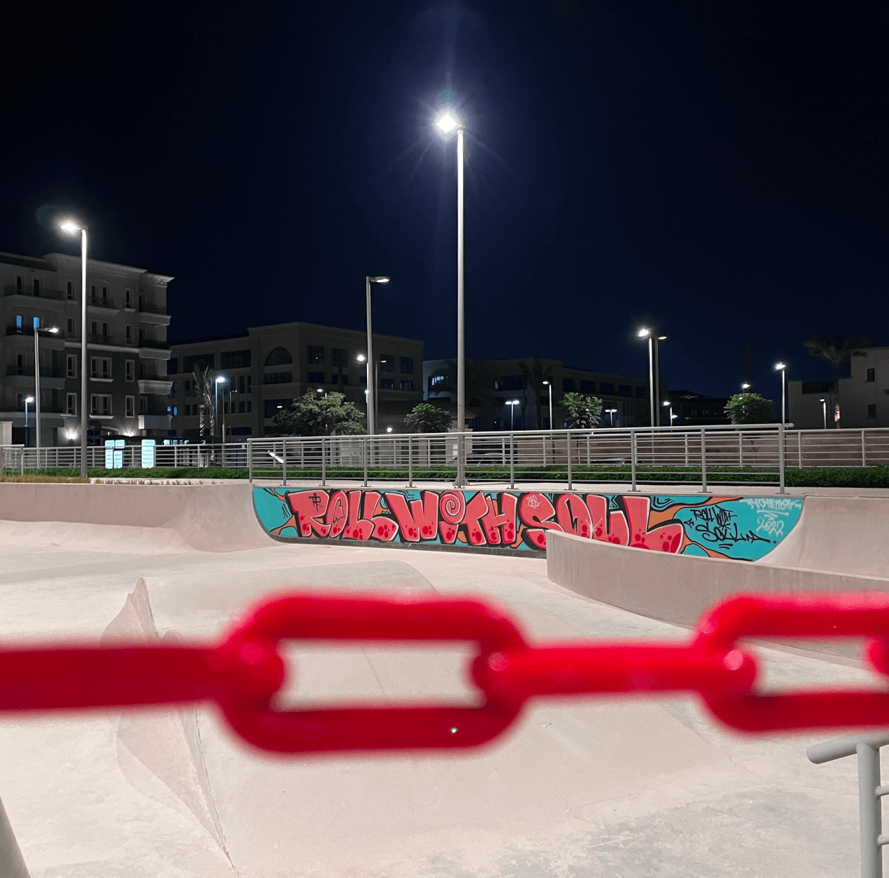A floodlit concrete skate bowl at night, its wall painted with the graffiti “Roll With Soul”